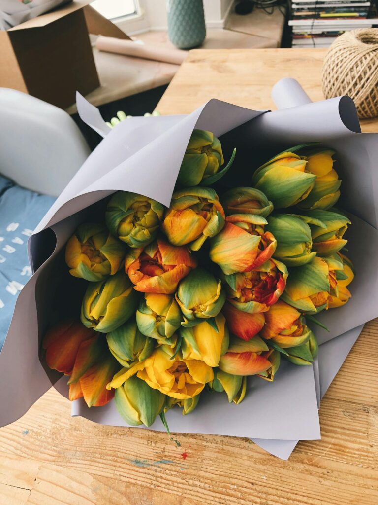 A bouquet of colorful tulips wrapped in paper, set on a wooden table indoors.