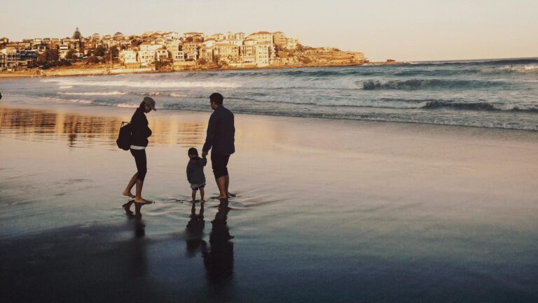 A family enjoying a peaceful walk along Bondi Beach during sunset, with city views in the background.