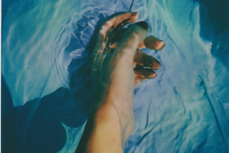 A hand gently moves through rippling water creating artistic reflections and refractions.