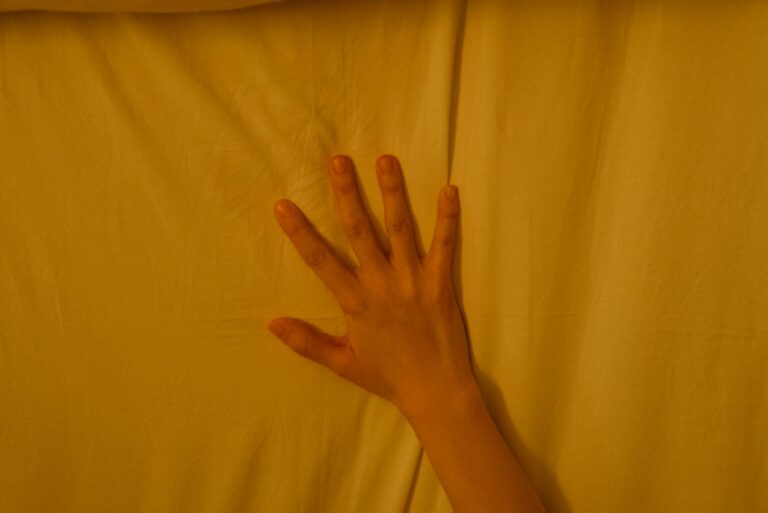 A hand gently touches a soft bed, capturing tranquility in warm lighting.