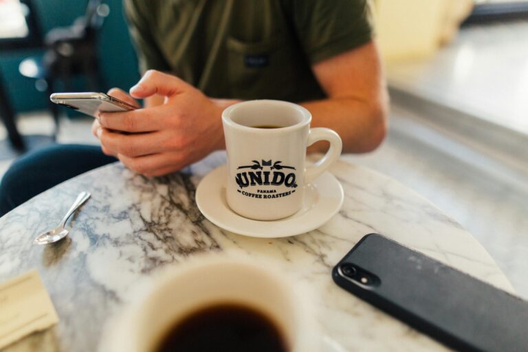 A person using a smartphone while enjoying coffee in a Panama café. Marble table adds elegance.