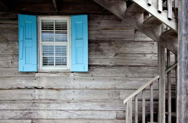 A rustic wooden cabin exterior with blue shutters and an outdoor staircase, showcasing simplicity and warmth.
