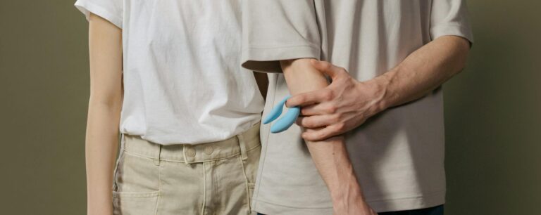 A young couple standing together indoors, holding a blue vibrator, symbolizing modern intimacy.
