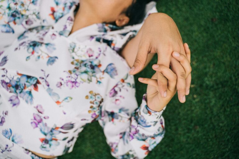 Close-up of a couple holding hands lying on green grass, expressing love and tenderness.