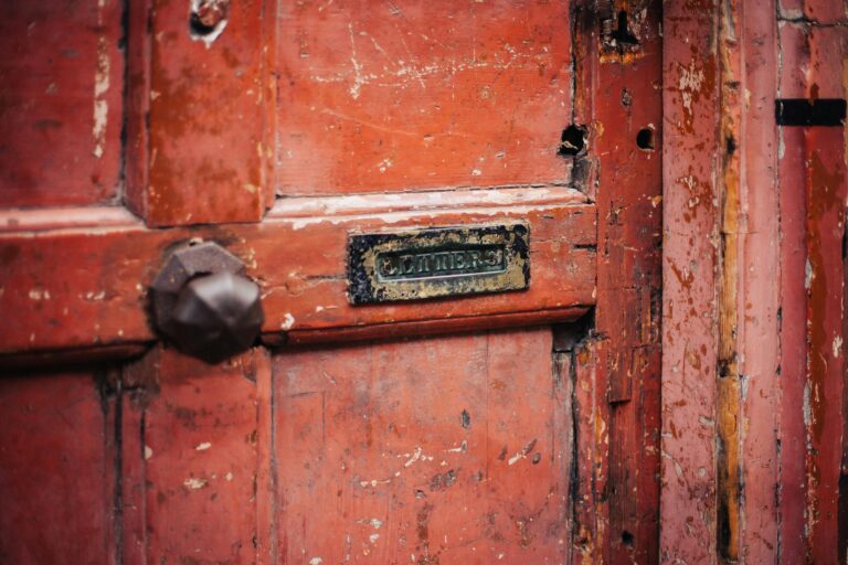 Close-up of a weathered wooden door featuring a vintage letterbox slot and peeling paint.