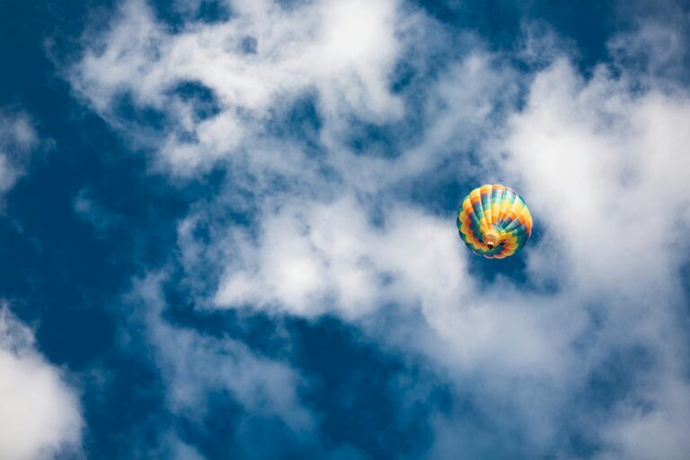 Colorful hot air balloon floating amid fluffy clouds on a bright summer day.