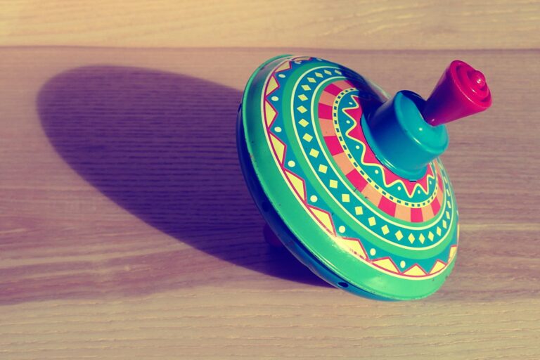 Colorful vintage spinning top toy casting a shadow on wooden surface.