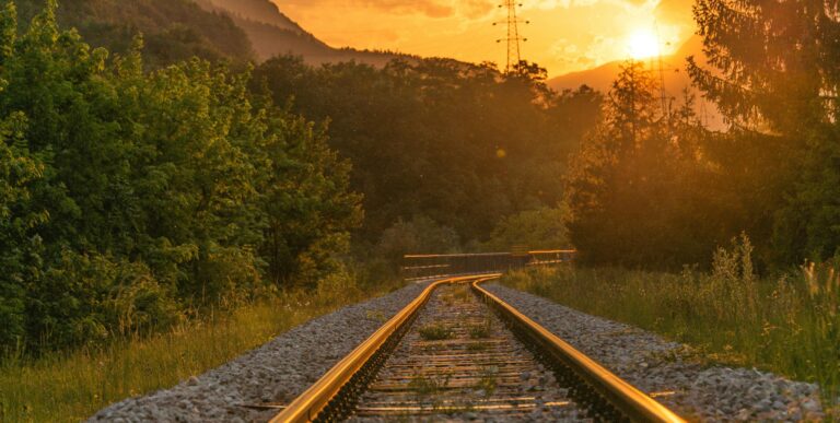 Golden sunset over railway tracks surrounded by lush greenery and mountains.