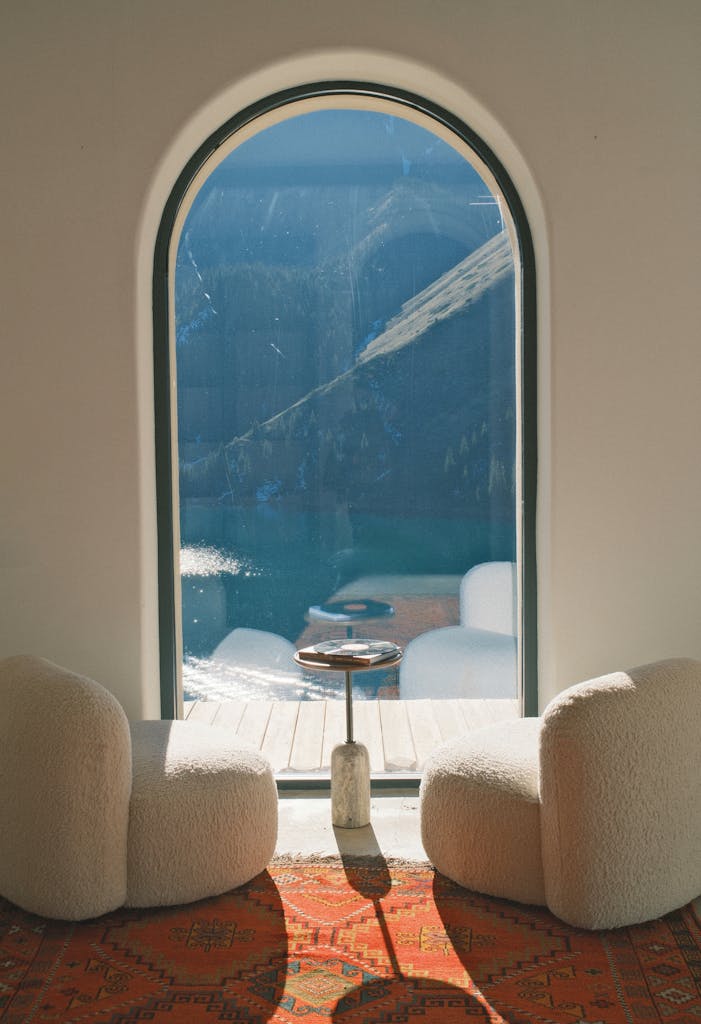 Relaxing interior with cushioned chairs overlooking a mountain view in Almaty Region, Kazakhstan through an arched window.