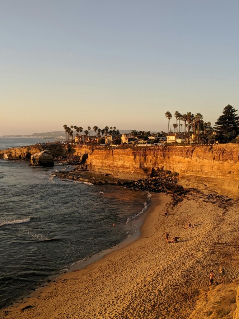 Serene sunset view of San Diego cliffs, beach, and sea with palm trees and golden sand.