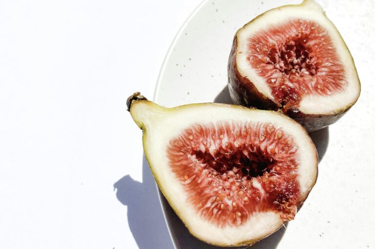 Sliced fresh figs on a white plate against a bright background, showcasing their juicy texture.