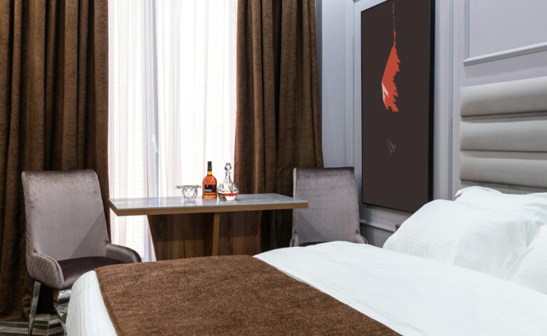 Soft bed against armchairs and table with carafe and bottle of liquor in light hotel room