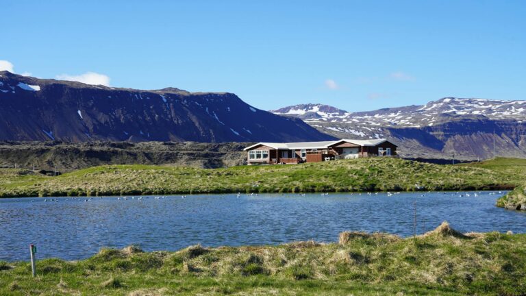 Stunning Icelandic landscape featuring a serene lake, rugged mountains, and a riverside cabin.