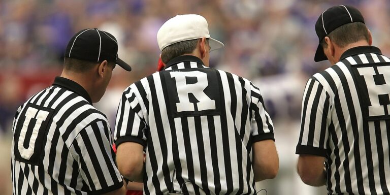Three referees in black and white striped uniforms at a sports event.