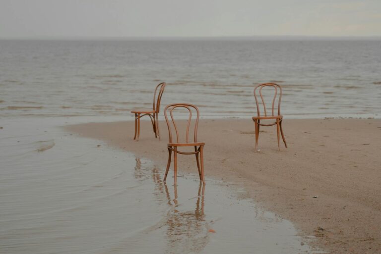 Three wooden chairs on a calm beach, creating a serene and minimalist coastal scene.