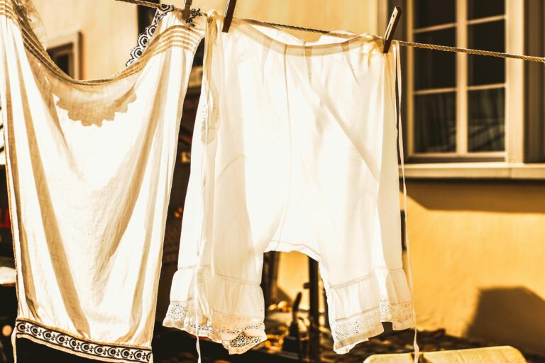 Vintage white clothing drying on a sunlit clothesline outside a window.