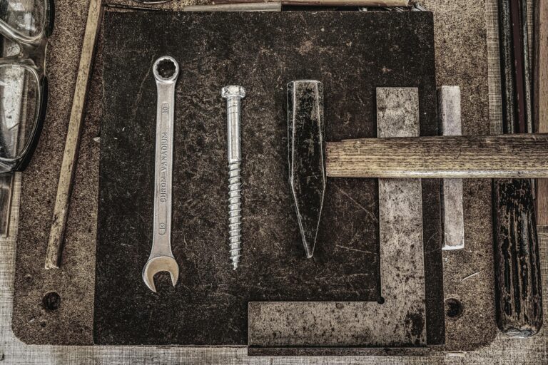 A collection of vintage workshop tools including a wrench, nail, and hammer displayed on a wooden table.