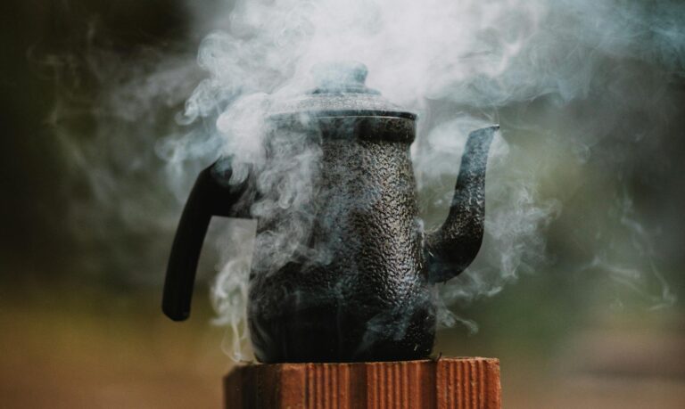 A steaming metal kettle sits on a wooden block, creating a misty ambiance outdoors.