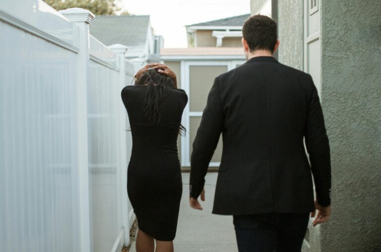 Back view of an interracial couple walking apart in an alley, suggesting breakup tension.