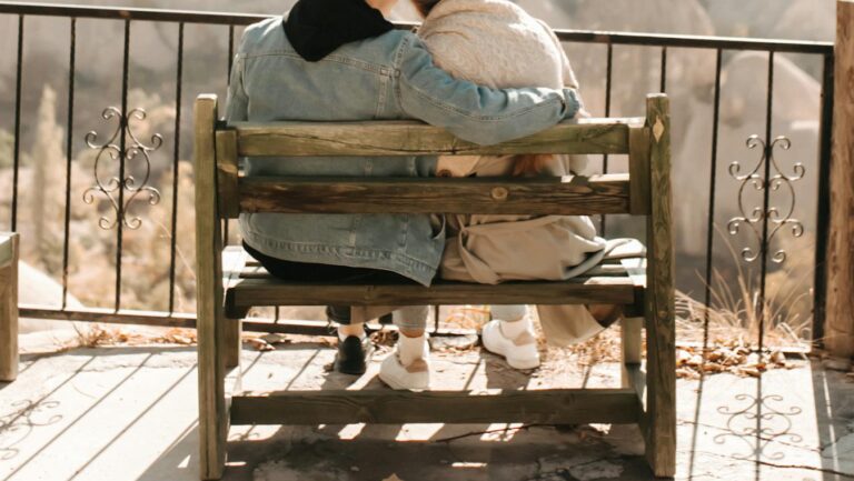 Couple hugging on a wooden bench overlooking a scenic view, creating a romantic and peaceful moment.